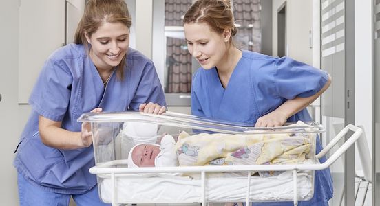 Two nurses in the obstetrics department look at a baby